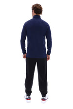 A man viewed from behind wearing a navy blue mock neck long-sleeve top, black sweatpants, and white sneakers with red and blue accents, set against a plain white background.