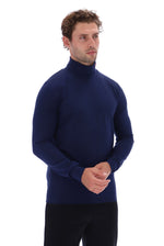 A man wearing a dark navy blue mock neck long-sleeve sweater and black trousers, standing against a solid white background.