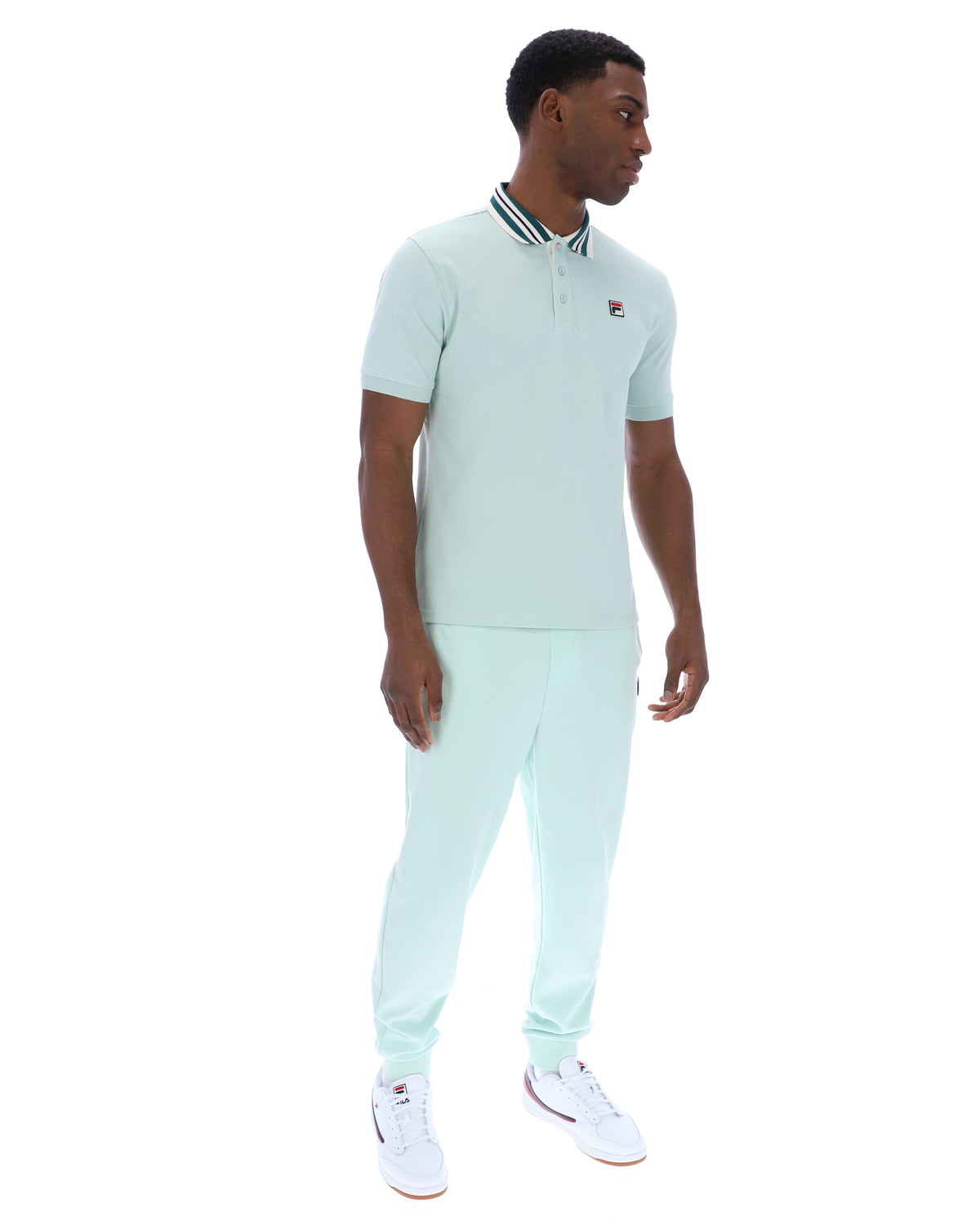 Man wearing a light green polo shirt with a small FILA logo on the chest, paired with matching joggers, against a white background
