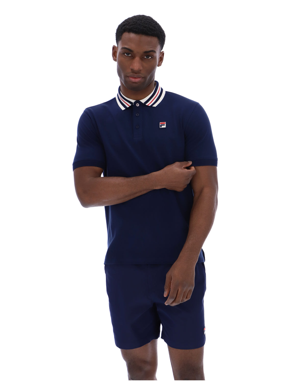 Man wearing a navy blue polo shirt and shorts set with a small logo on a white background