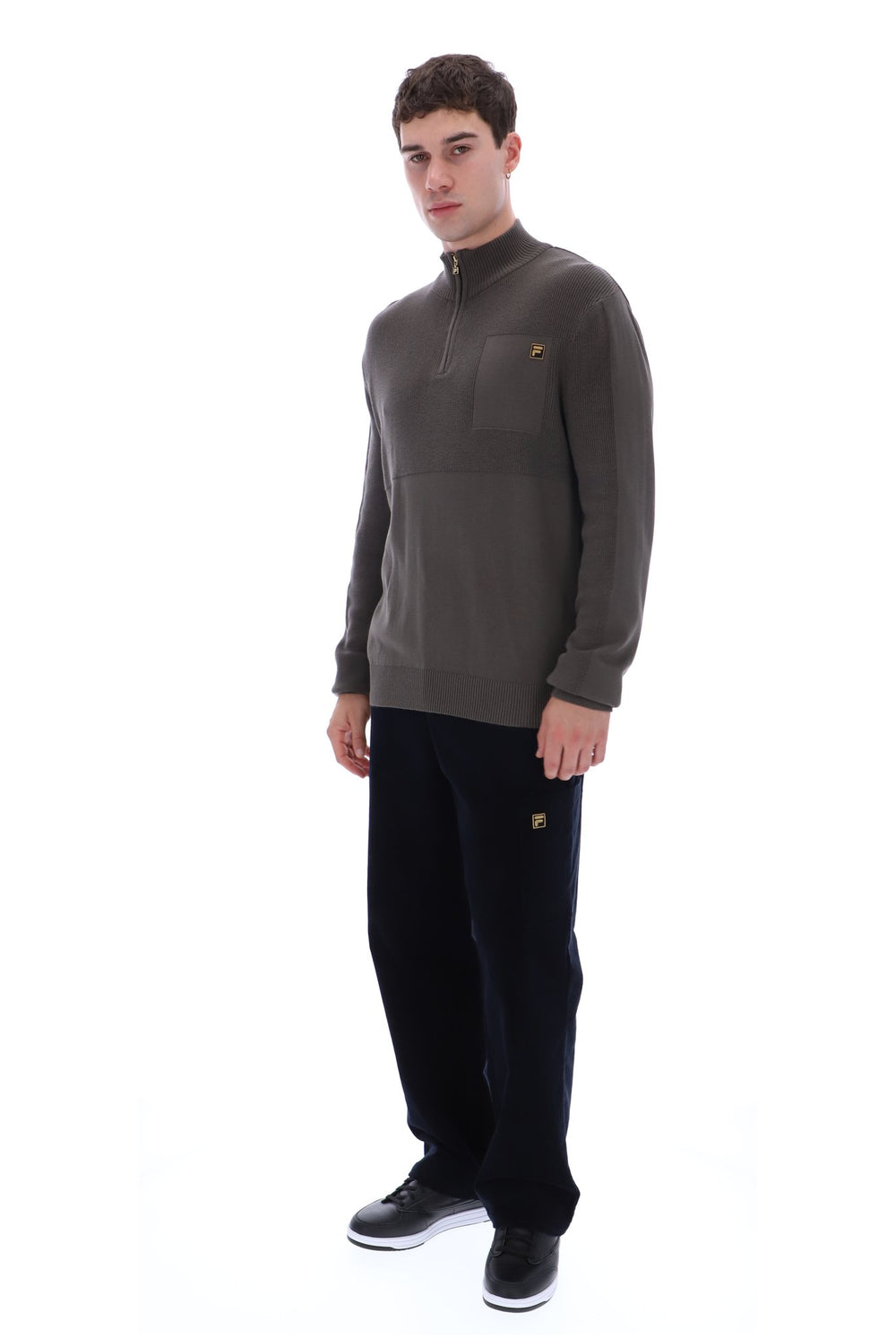 A man modeling a dark brown quarter-zip fleece pullover with a small embroidered logo on the left chest, paired with black sweatpants and black sneakers, against a solid white background.