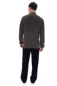 A man viewed from behind wearing a dark brown long-sleeve knit sweater and black trousers, standing against a plain white background.