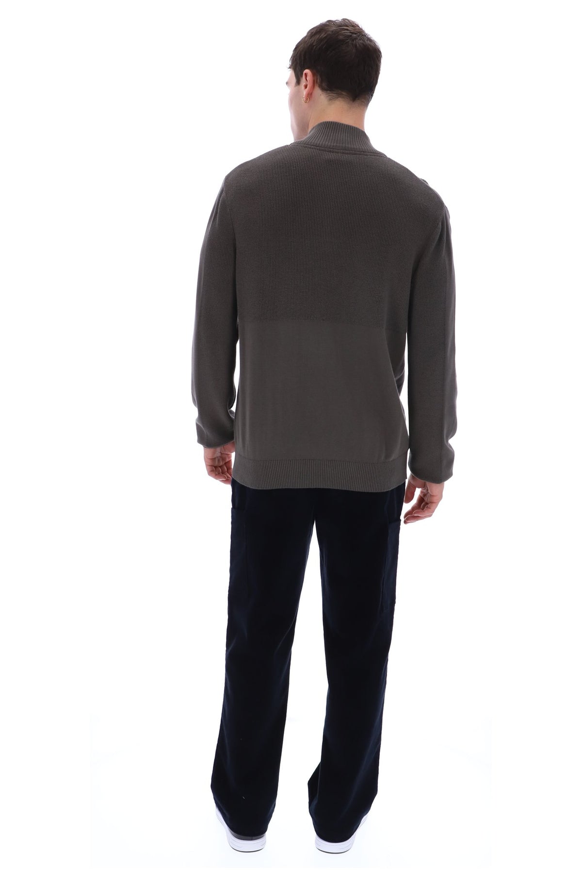 A man viewed from behind wearing a dark brown long-sleeve knit sweater and black trousers, standing against a plain white background.