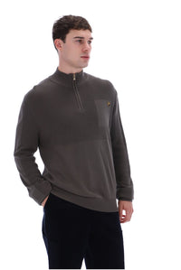 A man wearing a dark brown quarter-zip pullover sweater with a chest pocket and a small embroidered logo, paired with black pants, photographed against a solid white background.