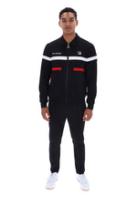 A man modeling a black FILA track suit with white and red stripe details on the chest and waist, paired with white sneakers, shot against a plain white background.