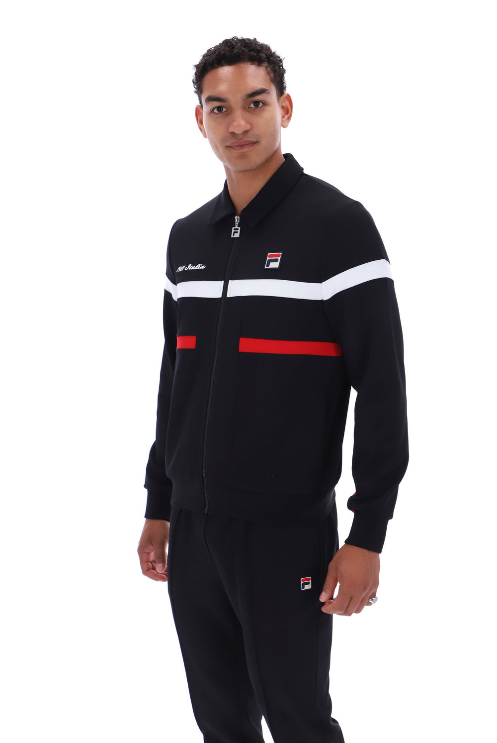 A man wearing a black FILA track jacket with white and red stripes, paired with matching black track pants, photographed against a plain white background.