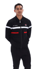 A man wearing a black Fila zip-up track jacket with white and red stripe accents, paired with black track pants, against a plain white background.