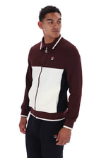 A man wearing a Fila colorblock zip-up track jacket in maroon, white, and black, paired with black track pants, against a plain white background.