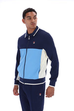 A man wearing a navy blue, light blue, and white color-blocked Fila track jacket and matching track pants, photographed against a solid white background.