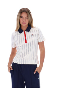 A woman modeling a white short-sleeve polo shirt with thin navy vertical pinstripes, a dark navy collar, and a red button placket. She is also wearing navy pants with a small Fila logo on the leg.