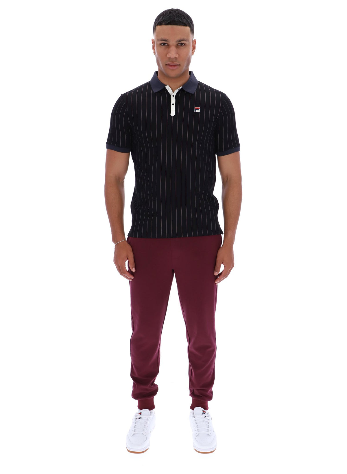 Man wearing a dark pinstripe polo shirt and maroon pants with a FILA logo on both, on a white background