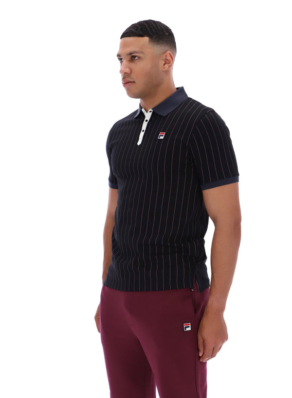 Man wearing a dark pinstripe polo shirt and maroon pants with a FILA logo on both, on a white background