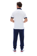 A man viewed from behind wearing a white short-sleeve polo shirt with thin navy vertical pinstripes and navy trim on the collar and sleeve cuffs, paired with navy jogger pants and white sneakers.