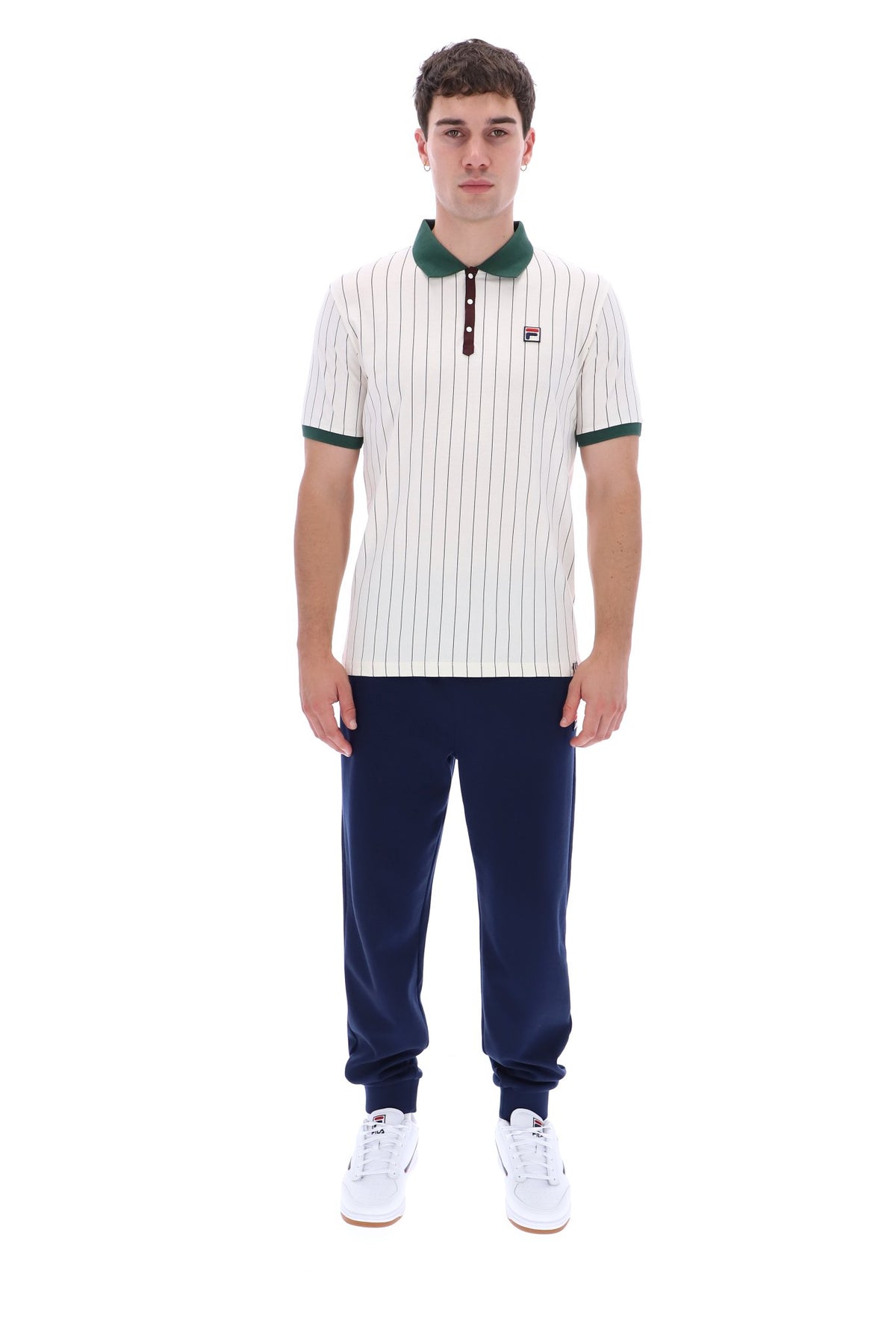 A man modeling a short-sleeve polo shirt with thin vertical navy stripes on an off-white base, featuring a dark green collar and sleeve cuffs, paired with navy pants and white sneakers against a plain white background.