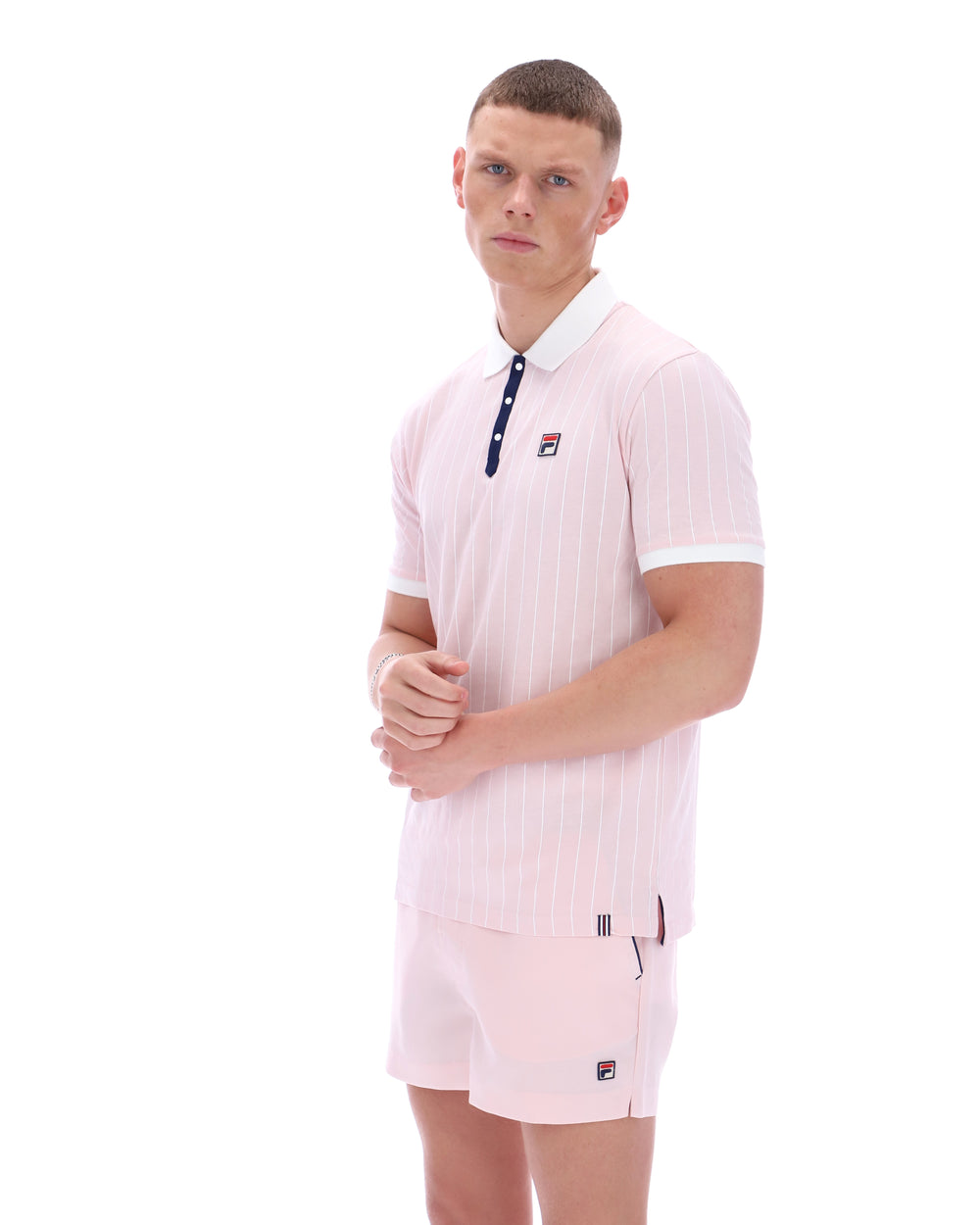 Man wearing a pink striped polo shirt and shorts with a visible brand logo on a white background