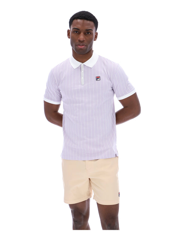 Man wearing a lilac striped polo shirt with a FILA logo on the chest, paired with beige shorts on a white background