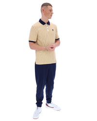 Man wearing a beige ribbed polo shirt and navy pants on a white background