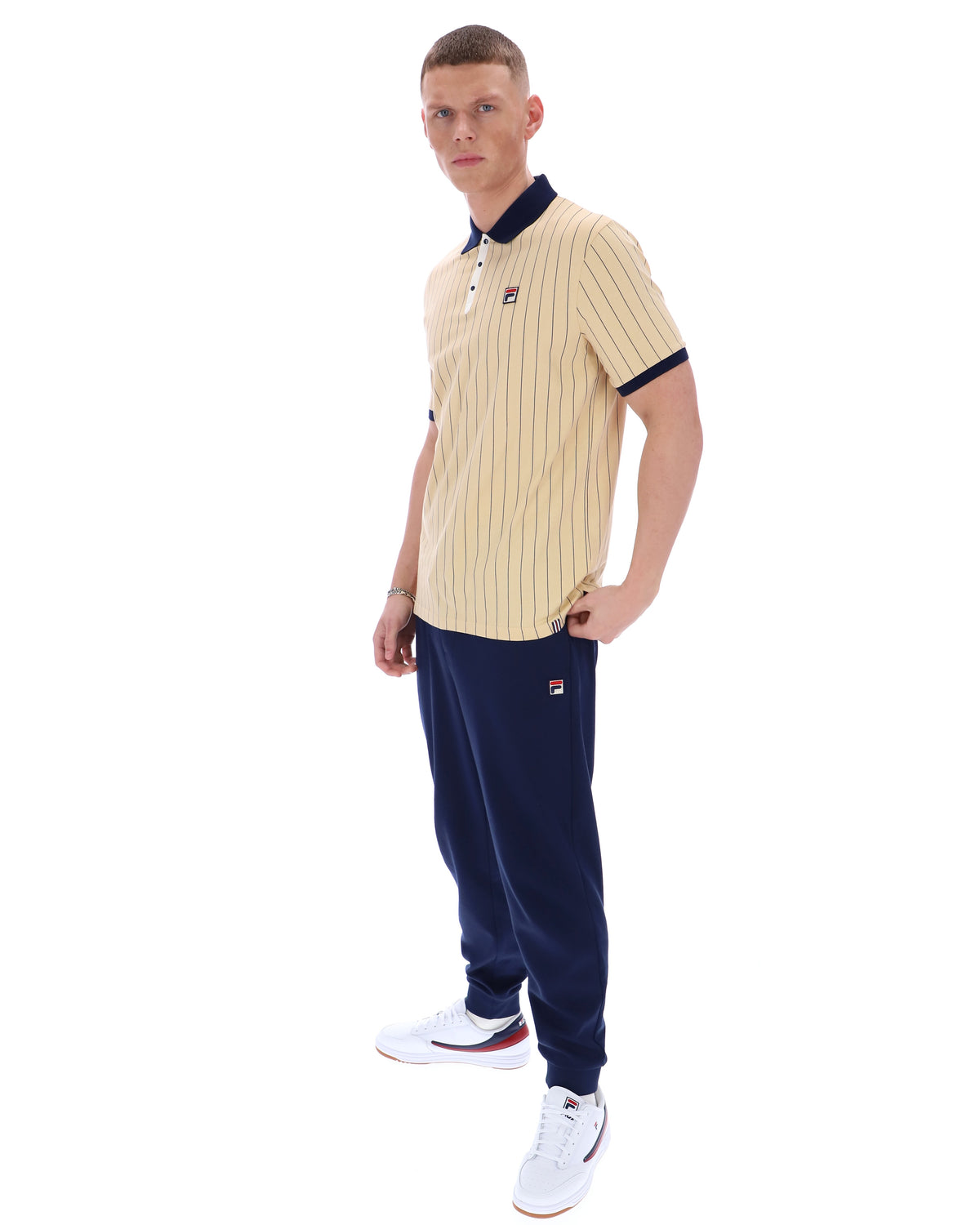 Man wearing a beige ribbed polo shirt and navy tracksuit pants on a white background