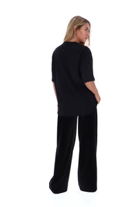 A woman wearing a black short-sleeve top and matching black wide-leg pants, shown from the back against a plain white studio background.
