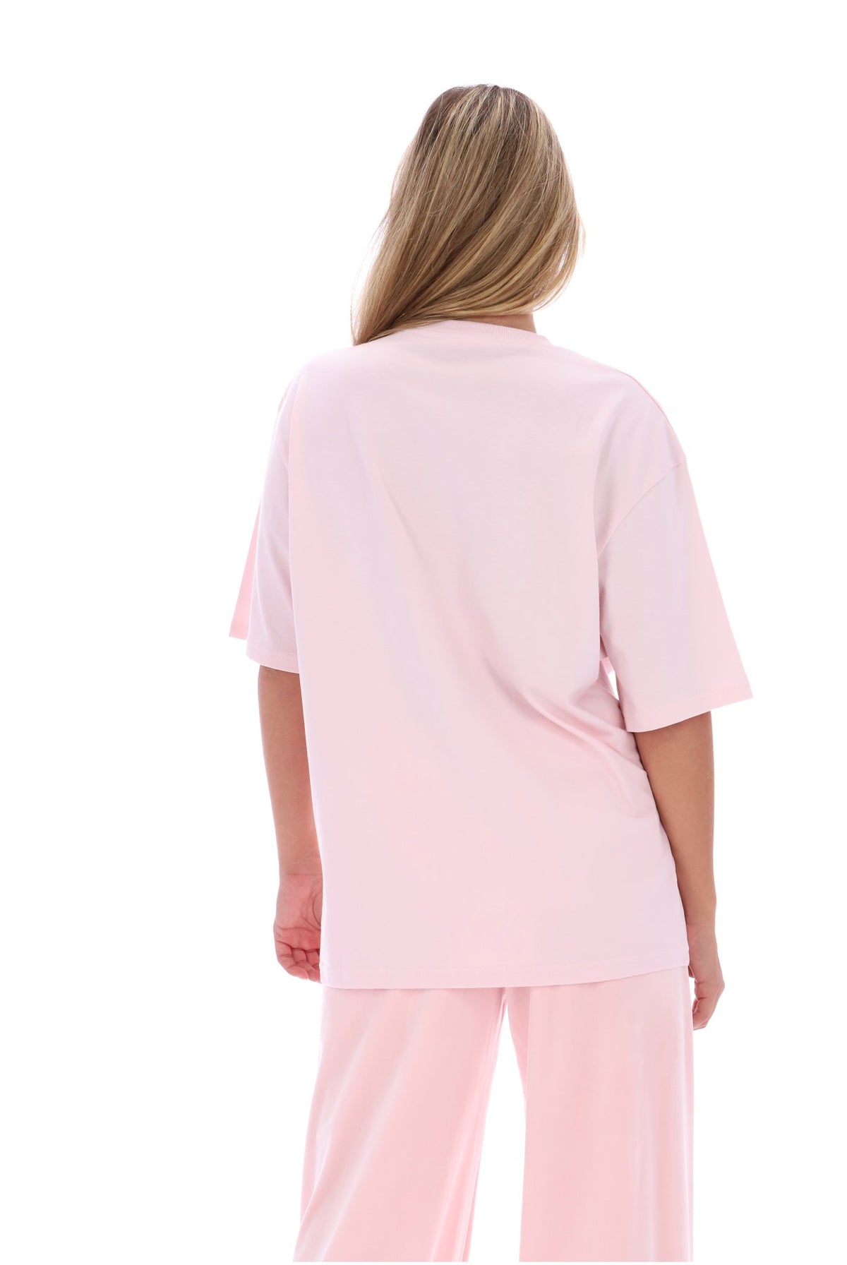 A woman viewed from the back wearing a light pink short-sleeve scrub top and matching pants against a plain white background.