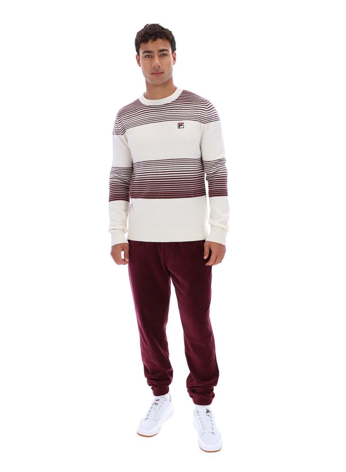 Man wearing a striped sweater and burgundy pants on a white background