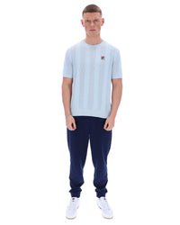Man wearing a light blue t-shirt and navy tracksuit pants on a white background