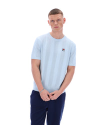 Man wearing a light blue t-shirt with a small logo on a white background