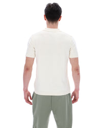 Person wearing a white polo shirt and green patterned pants on a white background