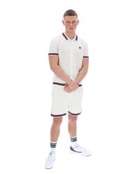 Man wearing a white polo shirt and shorts set with red accents on a white background