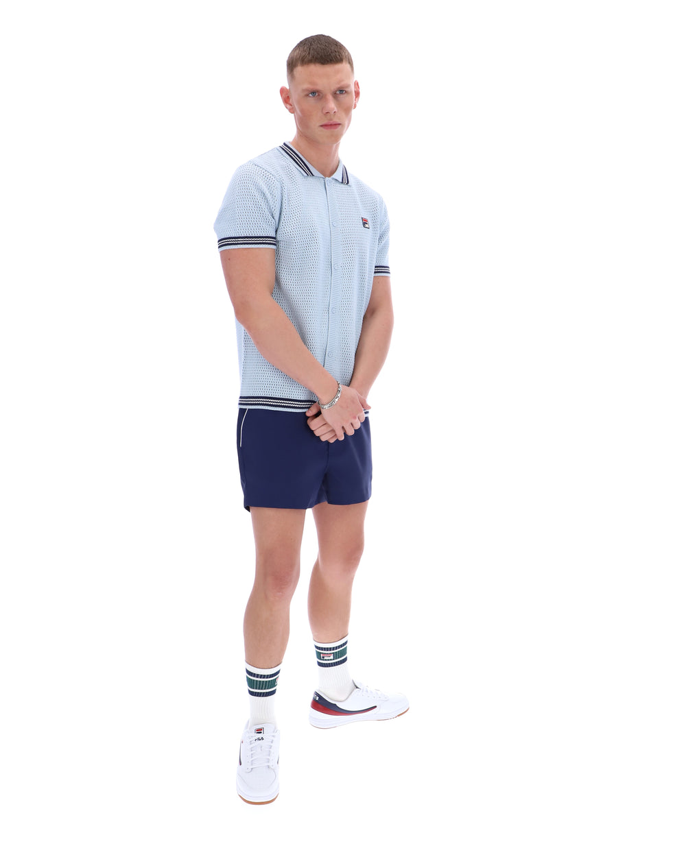 Man wearing a light blue patterned polo shirt with a FILA log on the chest and navy shorts, against a white background.