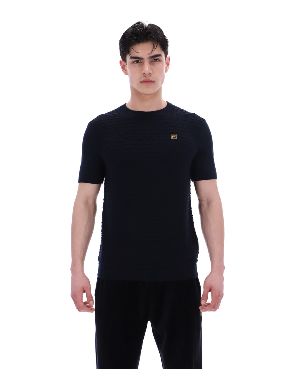 Man wearing a black t-shirt with a small FILA Gold logo on the chest on a white background