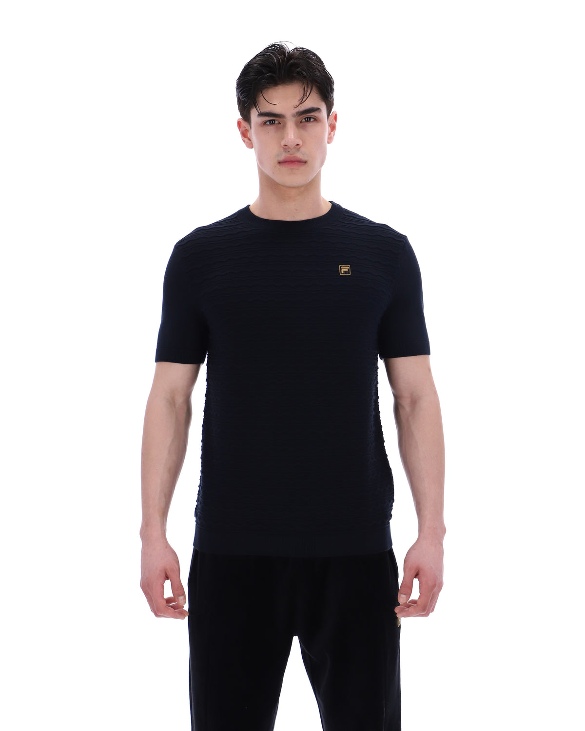 Man wearing a black t-shirt with a small FILA Gold logo on the chest on a white background