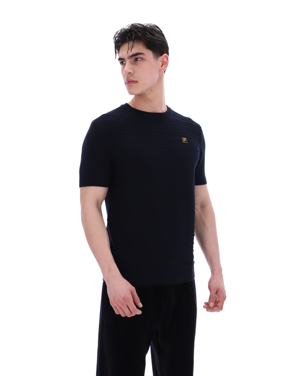 Man wearing a black t-shirt with a small FILA Gold logo on the chest with matching bottoms on a white background