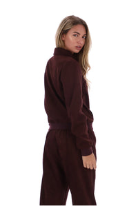 A woman modeling a matching burgundy fleece tracksuit, featuring a mock neck sweatshirt and matching jogger pants, shown from a three-quarters back view against a solid white background.