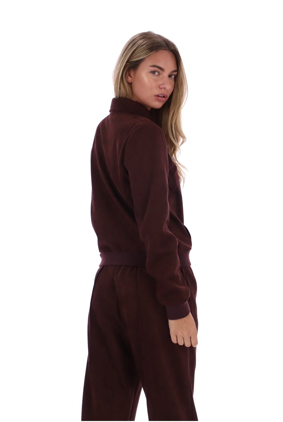 A woman modeling a matching burgundy fleece tracksuit, featuring a mock neck sweatshirt and matching jogger pants, shown from a three-quarters back view against a solid white background.
