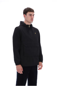 A man wearing a black hooded pullover jacket with a small gold embroidered logo on the left chest, paired with black pants, photographed against a solid white background.