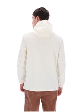 A man viewed from the back wearing a light cream hooded jacket and brown pants against a plain white background.