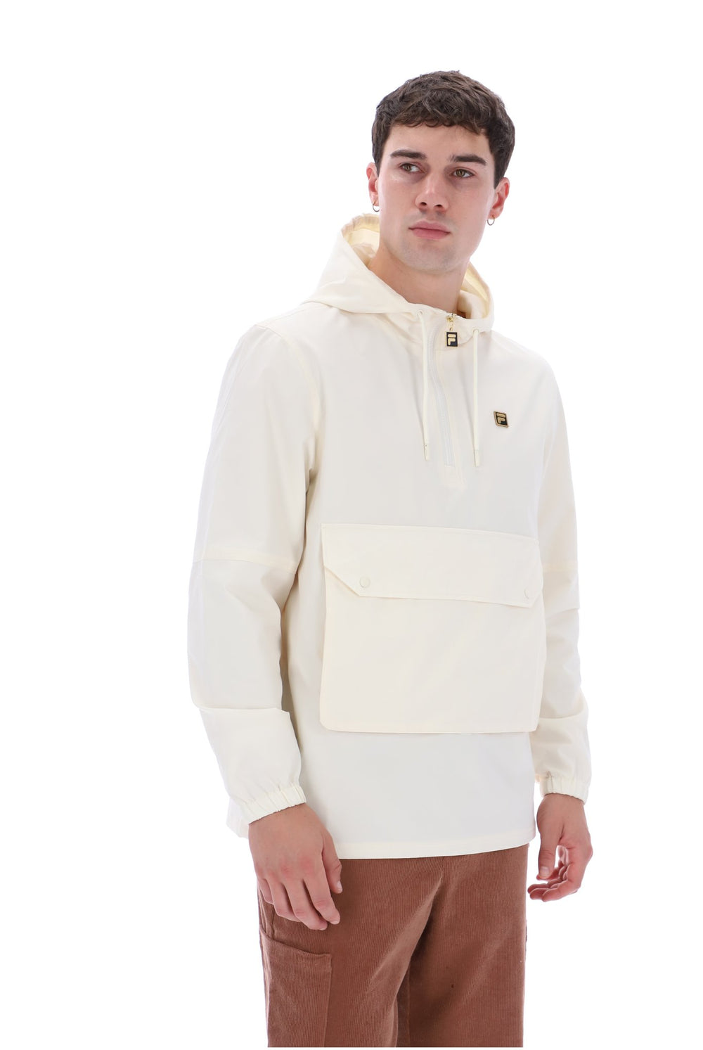 A man wearing a cream-colored pullover hoodie with a front flap pocket and drawstring hood, paired with brown pants, against a plain white background.