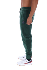 A side profile view of a person wearing dark green Fila jogger sweatpants and white sneakers with red and navy accents, set against a plain white background.