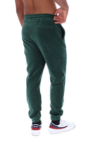 A man wearing dark green corduroy jogger pants, shown from the back. He is wearing white sneakers with red and navy accents and black socks, against a plain white background.