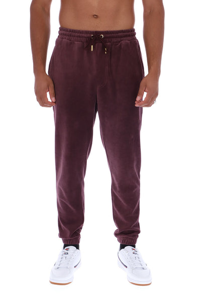 A man wearing dark plum corduroy jogger sweatpants with a drawstring waist and white sneakers, shown from the waist down against a plain white background.