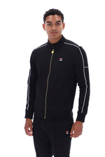 A man wearing a black Fila track jacket with white piping and a gold zipper, paired with matching black track pants, against a plain white background.