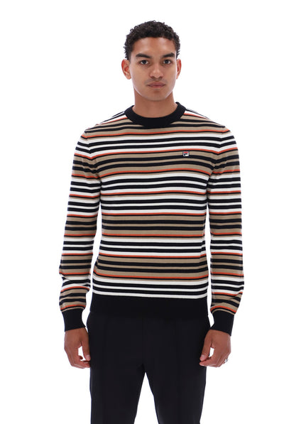 A man wearing a long-sleeve crewneck sweater with horizontal stripes in black, white, tan, and brown, paired with black trousers, photographed against a solid white background.