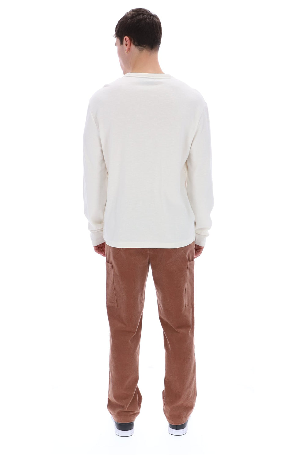 A man viewed from behind wearing a cream long-sleeve shirt and brown corduroy pants against a white background.