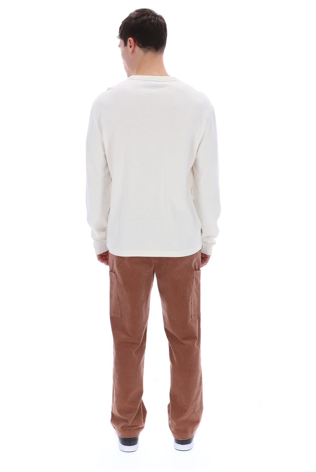 A man viewed from behind wearing a cream long-sleeve shirt and brown corduroy pants against a white background.