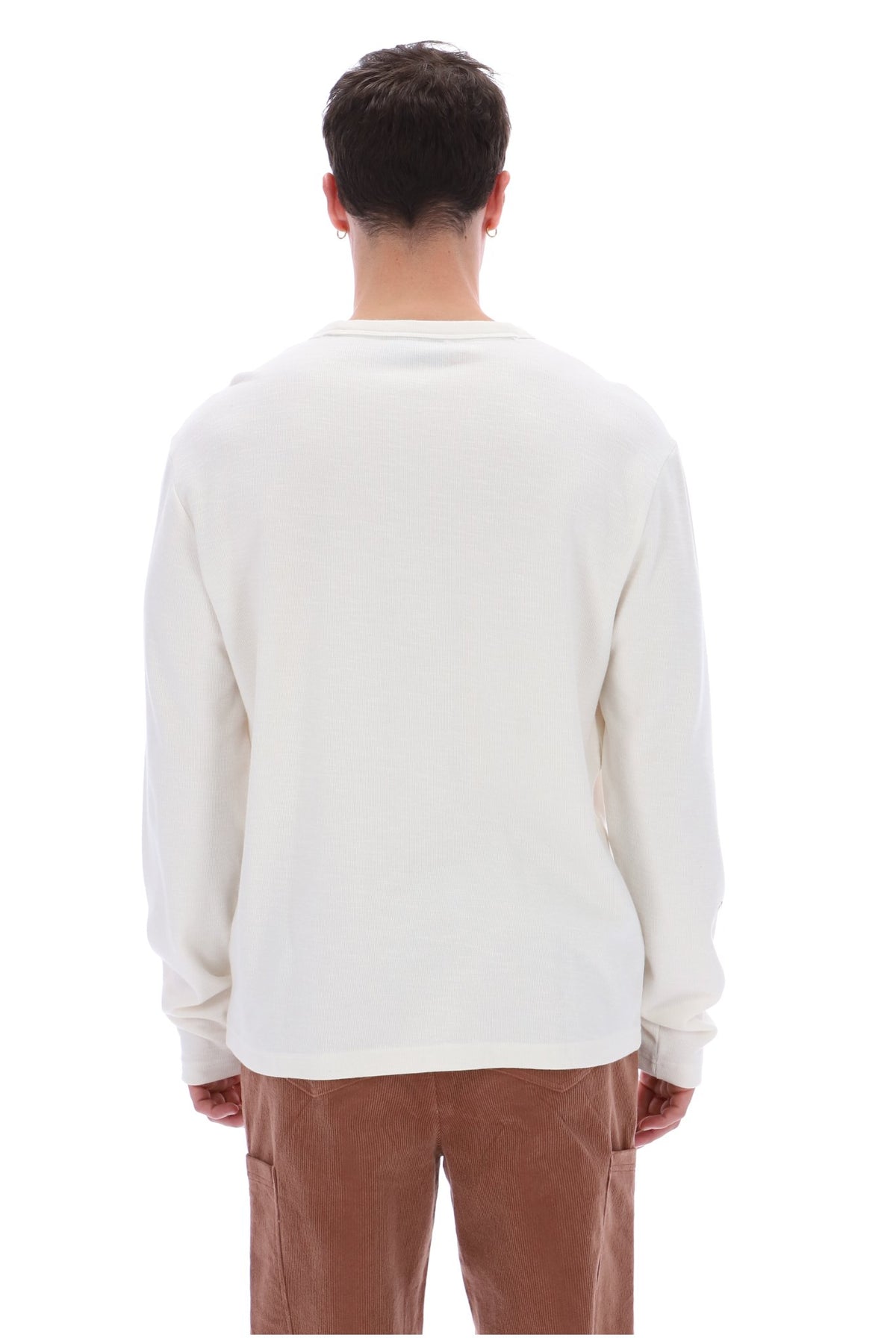 A man viewed from behind wearing a plain off-white long-sleeve crewneck shirt and brown pants, set against a solid white background.