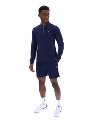 Man wearing a navy blue zip-up collared long-sleeve with a FILA logo on the chest, paired with matching shorts, on a white background