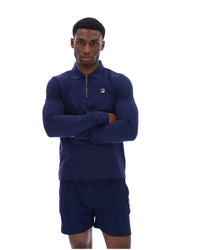 Man wearing a navy blue zip-up collared long-sleeve with a FILA logo on the chest, paired with matching shorts, on a white background