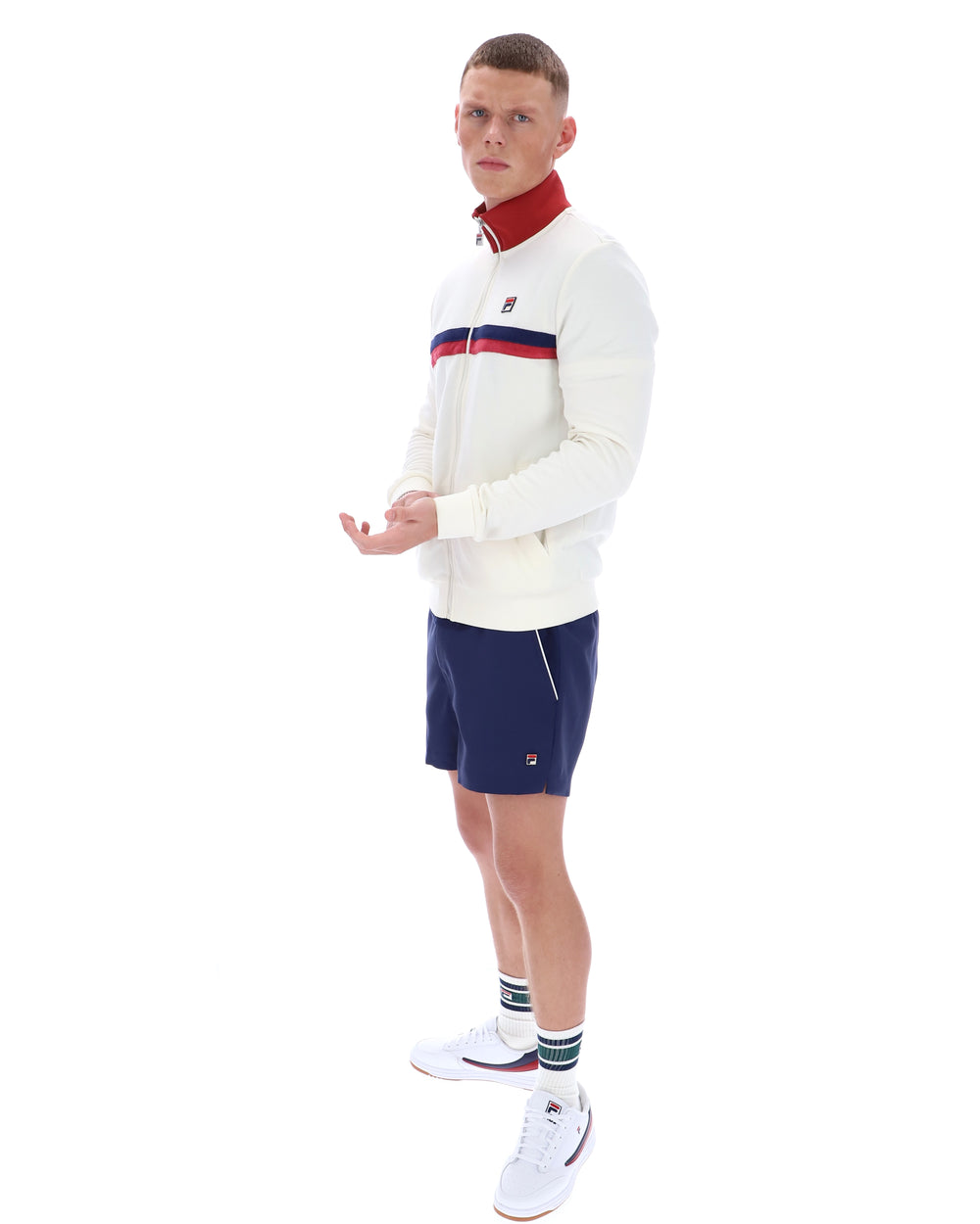 Man wearing a white sweater with red and blue accents and navy shorts on a white background