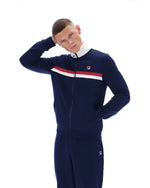 Person wearing a navy tracksuit with a red and white stripe on a white background